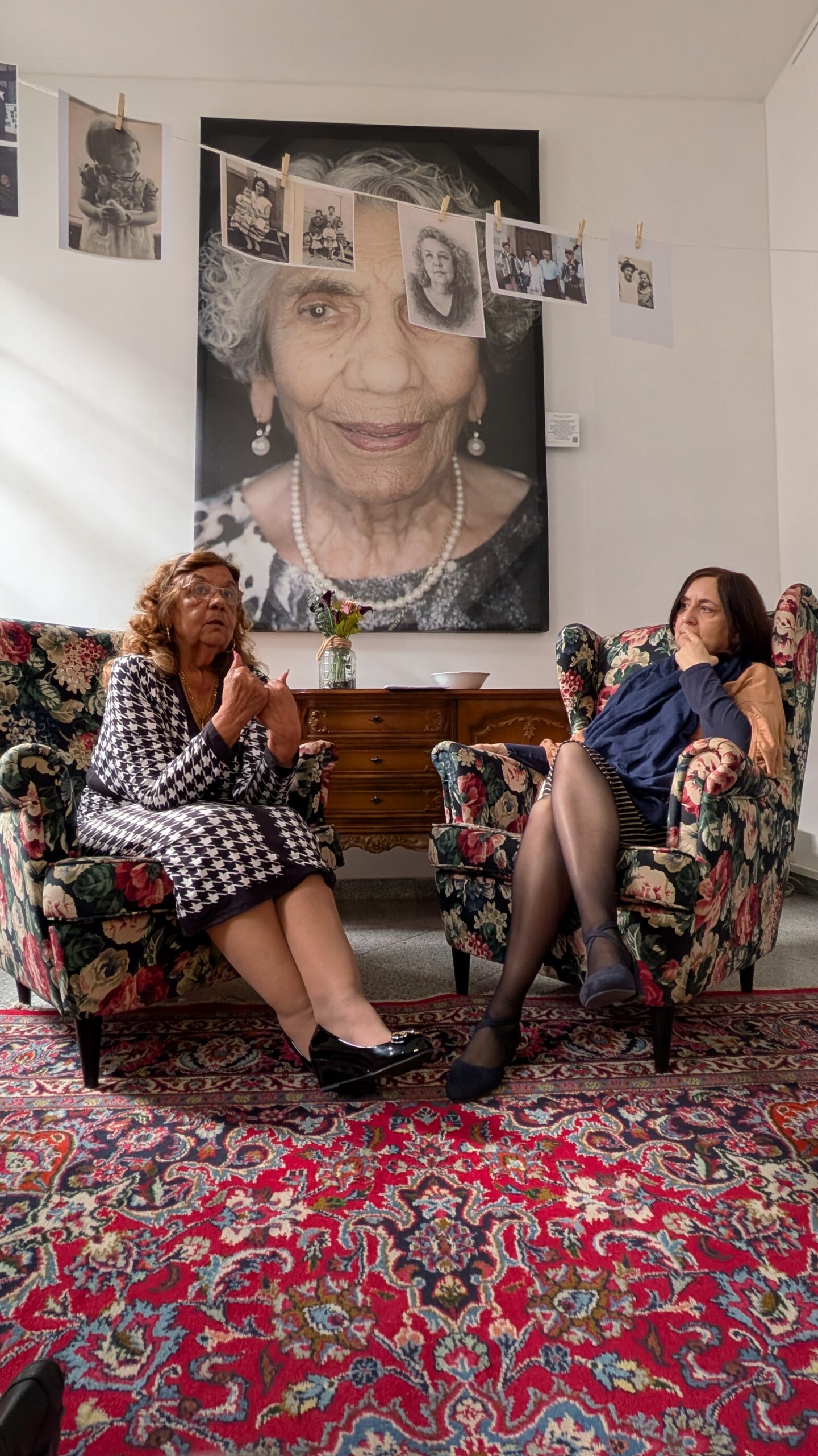 Manja und Monika sitzen vor dem Portrait von Zilli auf bunten Sesseln, über ihnen eine Wäscheleine mit Bildern von starken Sinti-Frauen